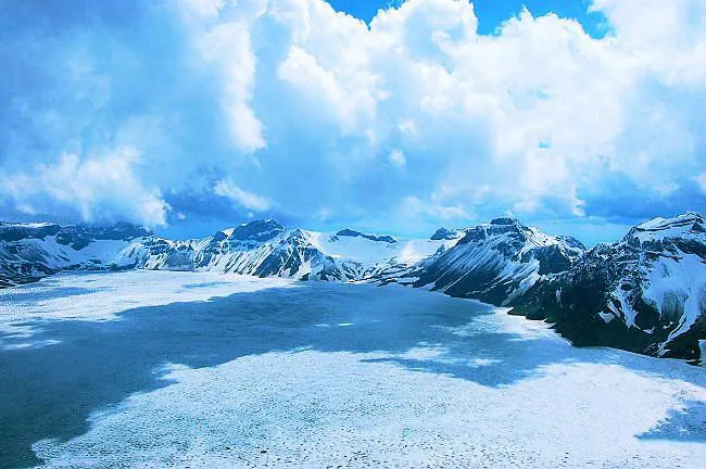 冰封期的天池：整潭水变成一块白蓝色的冰，雪沿着湖岸堆起来
