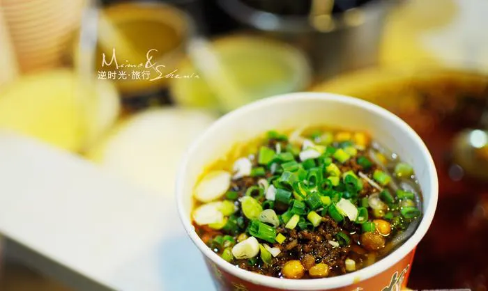A street-side bowl of sour-hot noodles: chilli oil, peanuts, pickles and scallions