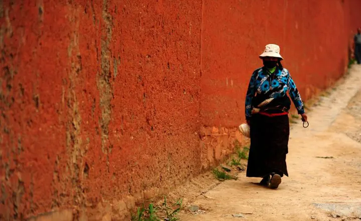 A woman in a wide-brimmed hat walking the red outer wall at Labrang, the circuit running along the other side