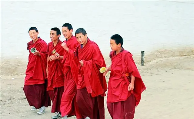 Young monks talking and laughing on open ground, red robes lifting in the wind