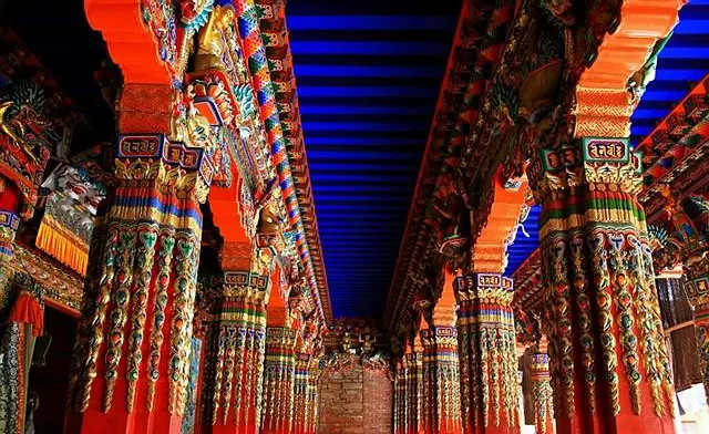 Painted pillars under a monastery porch, red and gold and blue stacked together — the palette the thangka shops work from