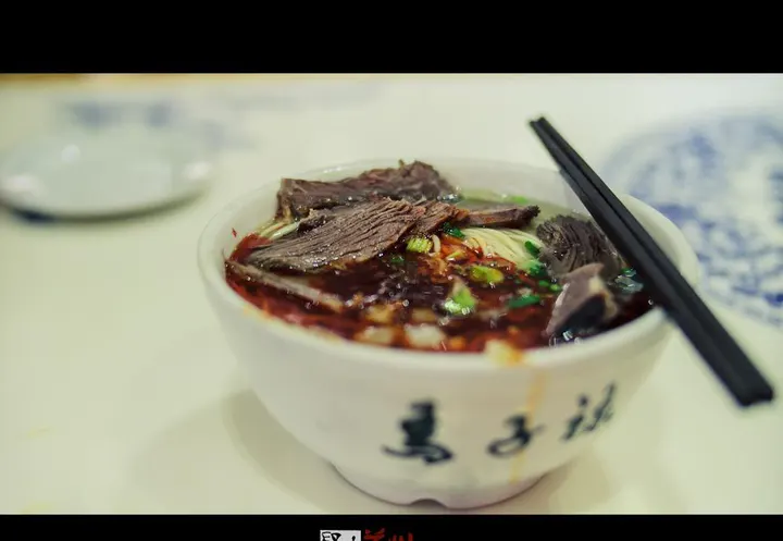 A bowl of Lanzhou beef noodles — clear broth, radish, chilli oil, coriander, noodles underneath