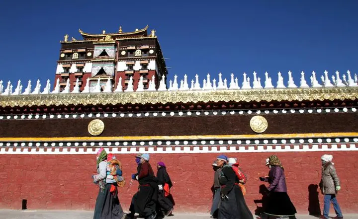 The low wall around the Milarepa Tower, white stupas along its top and pilgrims passing below