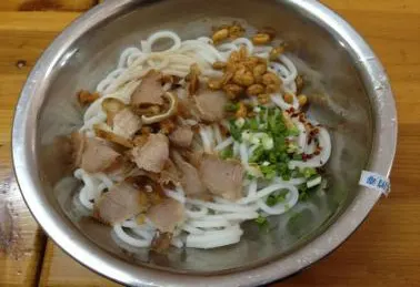 A bowl of rice noodles under braised meat and crackling