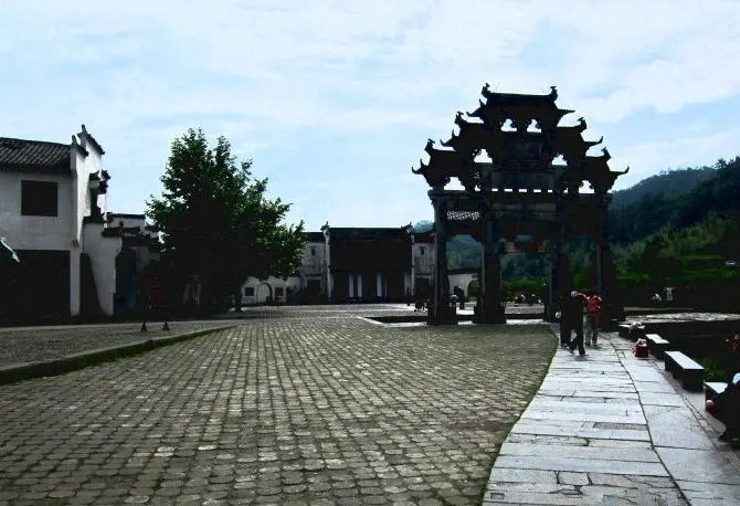 A stone memorial archway at a village entrance, three bays and five roofs, carved through under every eave