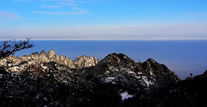 Snow-dusted summits above a flat bank of cloud, white still clinging to the north faces