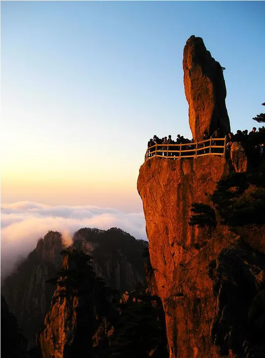 Low sun turning a granite pillar orange, the railing lined with people waiting for the light