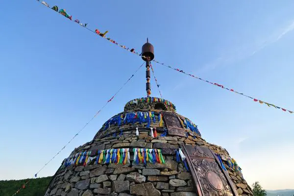 An ovoo on a ridge — stones piled into a cone, prayer flags running out from the top, a bronze bell above