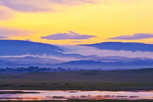 Dusk on the steppe — fog lying in bands across the far hills, a strip of water holding the last light