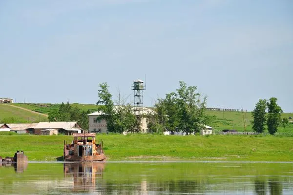 A landing stage on the border river — a barge, a watchtower, village roofs along the bank