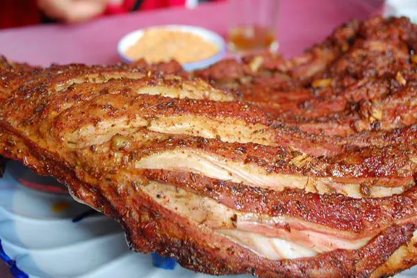 A whole roast rack, the crust blistered, a dish of dry dip behind it
