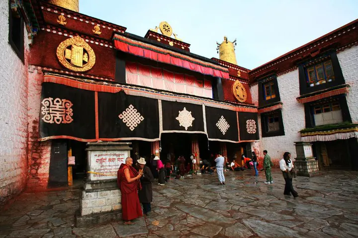 The Jokhang porch — black hangings with white endless knots, flagstones worn smooth