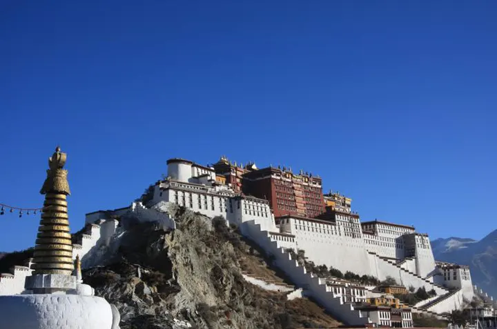 The Potala climbs Marpo Ri in stages, white below and red above; the chorten at its foot is where the kora begins