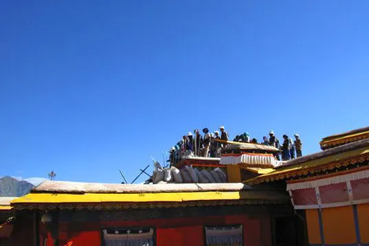 Figures on a roof terrace, a red wall and a band of yellow cornice below them