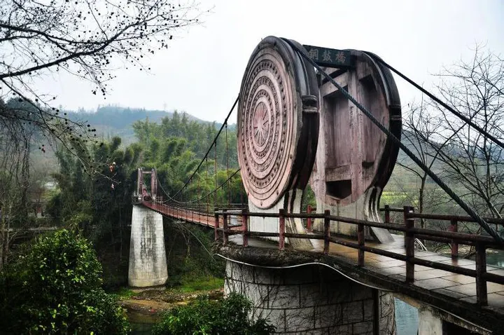 The bronze drum at the bridgehead: concentric rings around a sunburst, with the suspension bridge and valley behind