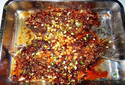 Zhangjiang grilled fish in a steel tray, fried soybeans and chopped fish mint over red oil