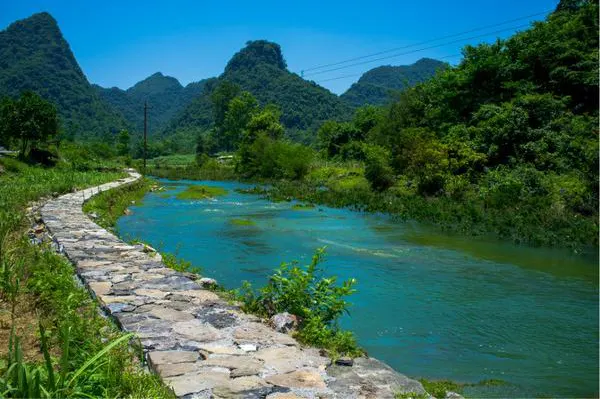 A stone-flagged path along the river, blue-green water on one side, bamboo and cone hills on the other