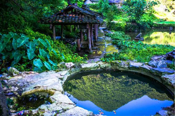 A stone-rimmed spring pool, still enough to hold the sky and the trees, with a small timber pavilion beside it