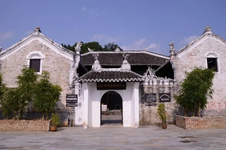 A courtyard behind stone walls, with a whitewashed gatehouse under dark tiles and two potted plants at the door