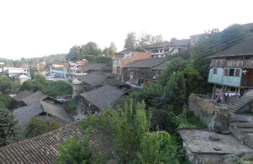 A hillside village of grey-tiled timber houses stacked upward, rooflines all at angles