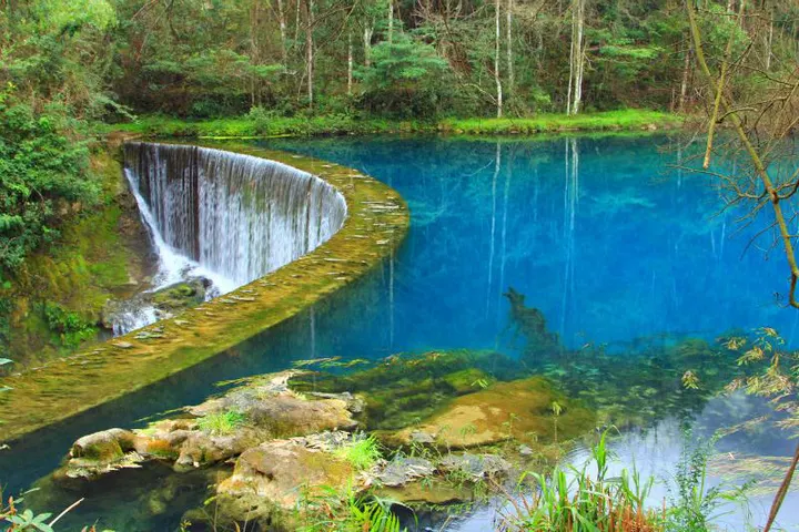 The curved weir spreading the river into a half-moon of white, over a pool of deep blue-green