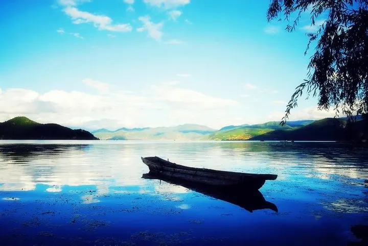 An empty canoe under the willows, the water flat enough to count clouds in