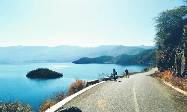 The loop road above the water: two riders, a guardrail, one small island offshore