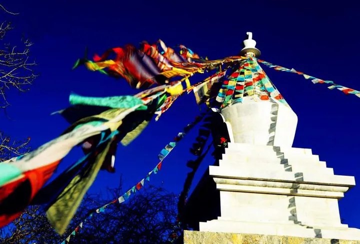 A white stupa strung with prayer flags, the wind pulling them flat