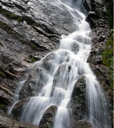 Water coming down a stacked rock wall, fanning out ledge by ledge over wet black stone
