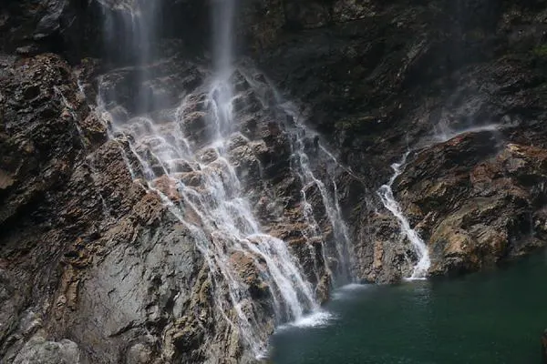 A pool in one of the valleys — water spreading down a wet rock face into water the colour of dark jade