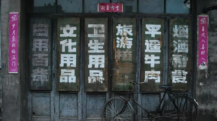 A shuttered shopfront lettered for daily goods, stationery, toiletries and Pingyao beef, with a bicycle leaning at the door