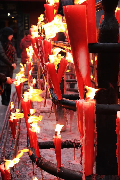 The candle rack outside a hall: red candles half burnt, wax running down the iron frame