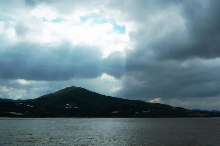 Mount Putuo from the water: a low ridge lying on the sea, light falling through a gap in the cloud