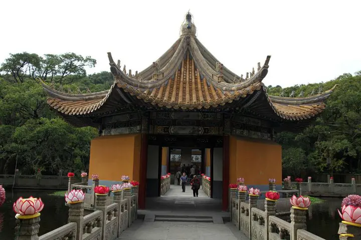 A gatehouse over water, its bridge balustrade lined with carved stone lotus lamps