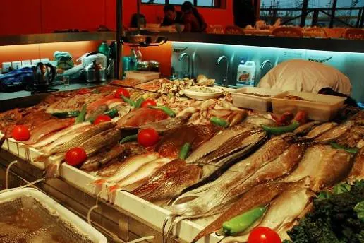 The counter of a seafood restaurant: whole fish on ice, an open kitchen behind