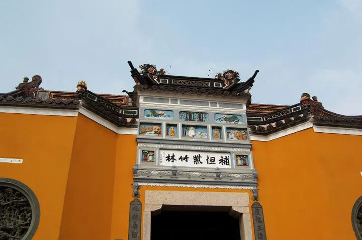The Purple Bamboo Forest gate: yellow walls, glazed tiles, five characters on the lintel and a row of painted panels above them