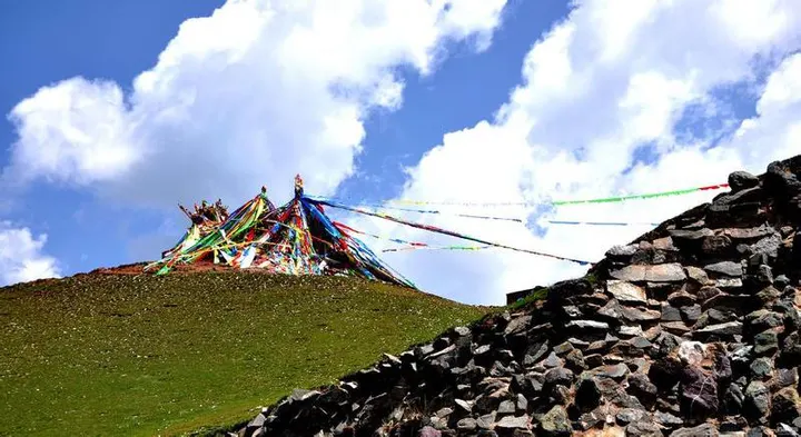 山坡上的经幡堆和玛尼石墙，经幡从堆顶向四面拉出去，天上是积云