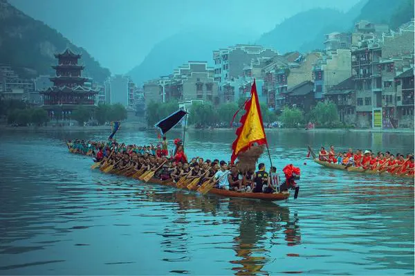 Dragon boats passing the old town, a pagoda on the ridge behind