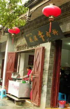 A mutton rice-noodle shop at a lane mouth, red lanterns over the door, the owner busy at the cart