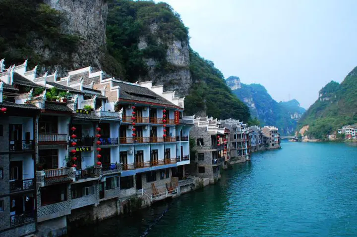 Riverside houses on the south bank: white walls, timber windows, red lanterns, a sheer cliff behind